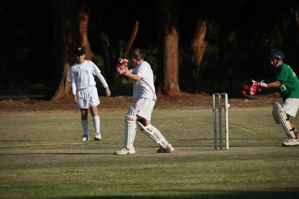 A junior batsman playing a shot with a wicketkeeper behind the stumps